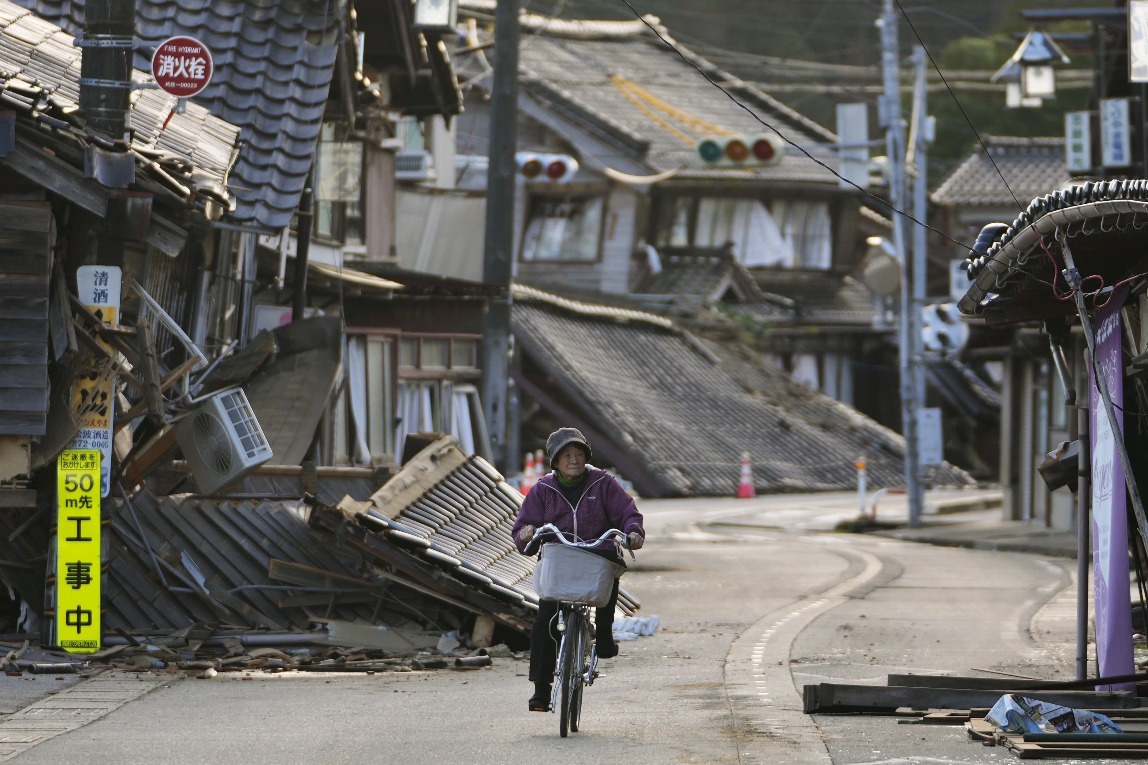 2024年1月2日，日本能登镇，一名女性骑着自行车通过地震后破损的街道。(AP Photo / Hiro Komae)